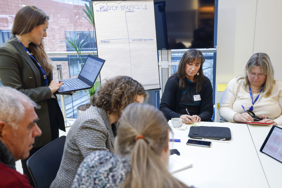 Woman with a laptop and people discussing around a table
