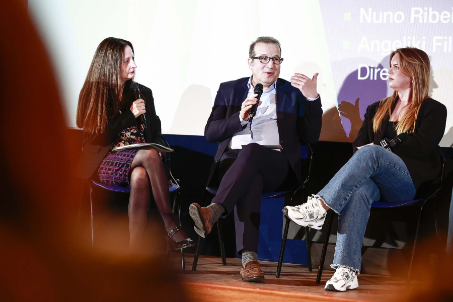 Panel discussion, man speaking on microphone, 2 women watching